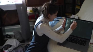 Genç bir kadın dizüstü bilgisayarına, dağınık eşyalarla dolu sıcak ve rahat bir atmosferde odaklanır.