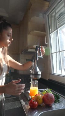 Neşeli ve neşeli bir mutfakta genç bir kadın taze narenciye suyu yapmak için büyük bir hevesle meyve sıkacağı kullanır.