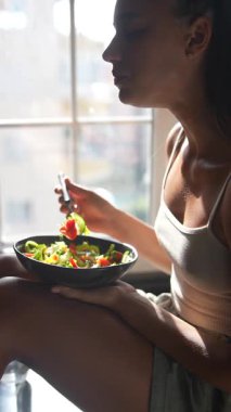 Bir kadın gerçekten parlak, güneşli bir odada canlı ve renkli bir salatanın tadını çıkarıyor, sağlıklı beslenme alışkanlıklarını teşvik ediyor.