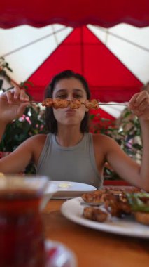 Bir kadın nefis bir şekilde ızgara tavuk şişi yiyor. Hem de davetkar, büyüleyici bir açık hava yemek ortamında.