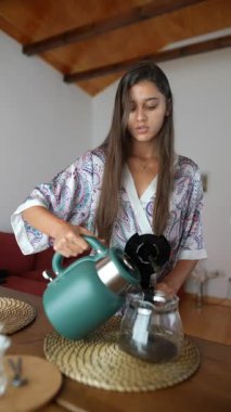 Huzurlu ve modern bir ortamda, bir kadın nazikçe çaydanlıktan cam bir kavanoza buharlı çay döker.