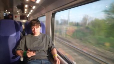 Genç bir gezgin trende manzaralı bir gezinti yapıyor, akıllı telefon kullanıyor ve pencereden doğayı seyrediyor..