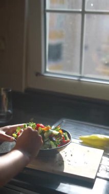 Bir kadın parlak, neşeli mutfağında canlı ve renkli bir salata hazırlıyor, sağlıklı beslenme alışkanlıkları sergiliyor.