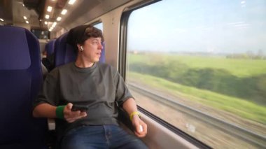 Genç bir gezgin, doğanın çarpıcı güzelliğine kendini tamamen kaptırmış bir şekilde trenin penceresinde rahatlıyor.