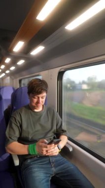 Genç bir adam, sakin ve manzaralı tren yolculuğunun tadını çıkarırken telefonuyla çok meşgul.