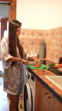 Genç bir kadın şık bir mutfakta sebze hazırlıyor. Yemek pişirme becerilerini ve mutfak ortamını gösteriyor..