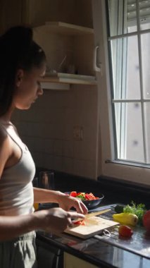 Bir kadın parlak bir mutfakta renkli sebzeler hazırlıyor. Mutfak yeteneklerini büyük bir hevesle sergiliyor.