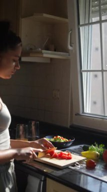 Bir kadın güneşli bir mutfakta taze sebzeler hazırlıyor, sağlıklı yemek ve canlı tatları vurguluyor.