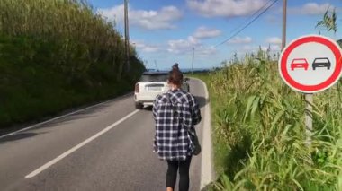 Bir insan, yemyeşil yemyeşil ve açık mavi gökyüzü ile çevrili, dolambaçlı, manzaralı bir yolda rahatça dolaşır.