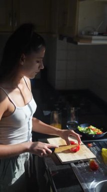 Genç bir kadın mutlu bir şekilde güneşli mutfağında renkli sebzeler hazırlıyor ve sağlıklı pişirme tekniklerini vurguluyor.