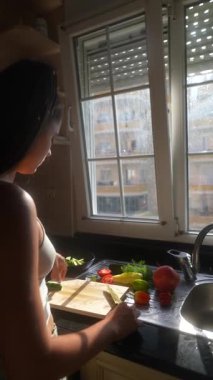 Sıcak güneş ışığıyla aydınlatılmış mutfak tezgahında özenle taze, renkli sebzeler hazırlayan bir insan.