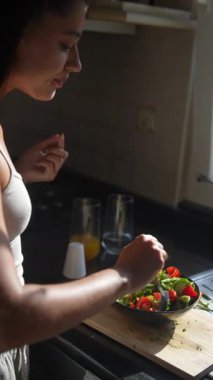 Bir kadın güneşli bir mutfakta taze bir salata hazırlıyor, canlı malzemeler sergiliyor ve sağlıklı besleniyor..