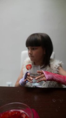 Neşeli bir çocuk masada oturmuş, elinde canlandırıcı bir bardak su ve canlı bir çilek dilimi tutuyor.