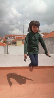 Kaygısız bir çocuk neşeli bir şekilde ipten atlar güneşli bir çatıda, eğlencenin ve eğlencenin neşesine dalmıştır.