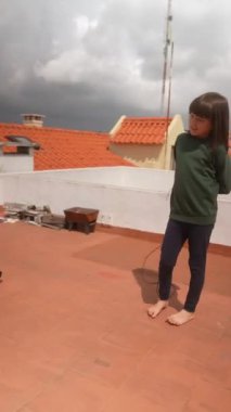 Genç bir çocuk bulutlu bir gökyüzünün altında canlı ve renkli bir çatıda neşeyle ip atlıyor.