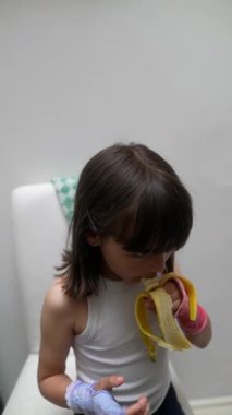 Genç bir çocuk mutlu bir şekilde olgun bir muz yiyor. Saf masumiyet ve neşe sergiliyor. Rahat ve davetkar bir ortamda.