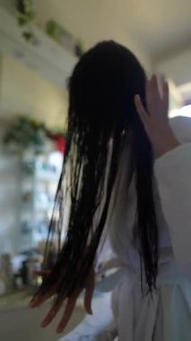 Bir kadın uzun, ıslak saçlarını şekillendirirken huzurlu bir banyoda rahat bir bornoz giyerken zarifçe görülüyor.