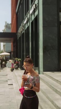 Canlı çiçekli kıyafetli şık genç bir kadın modern bir şehir ortamında dinlenirken içkinin tadını çıkarıyor.