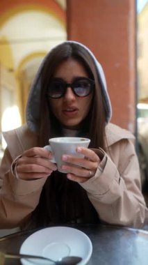 Genç bir kadın, büyüleyici bir açık kafe atmosferinde dinlenirken lezzetli kahvesini yudumluyor.