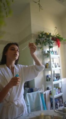 Doğal ışık ve yemyeşil ile dolu sakin bir banyoda bir kadın titizlikle cilt bakımını yapar.