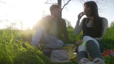 Canlı yeşillik ve yumuşak güneş ışığıyla çevrili, açık havada sakin bir pikniğin tadını çıkaran sevimli bir çift.