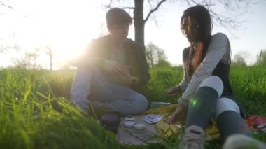 Mutlu bir çift, canlı yemyeşil ve sıcak güneş ışığıyla çevrili keyifli ve keyifli bir piknik anını paylaşır.