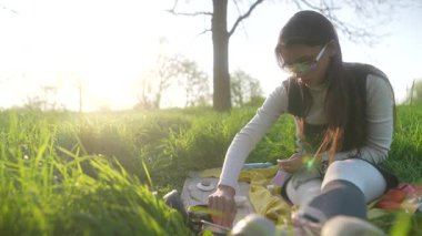 Bir kadın dışarıda huzurlu bir anın tadını çıkarıyor. Güneşin sıcaklığında güneşlenirken yaratıcı bir aktiviteyle meşgul oluyor.
