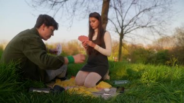 Sevgi dolu bir çiftin güneşli bir günde çimenli bir parkta kağıt oynayıp eğlendiği huzurlu ve huzurlu bir an.