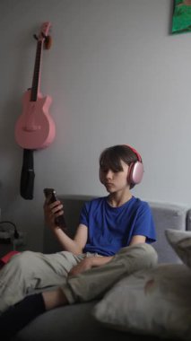 Genç bir çocuk evde rahatça dinleniyor, kulaklık takarken medyanın çeşitli şekillerine dalmış.