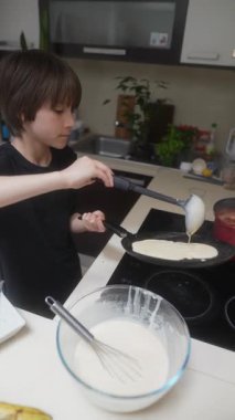 Parlak ve modern bir mutfakta, genç bir çocuk, etkileyici yemek pişirme yeteneğini gururla sergileyerek, ustalıkla krep çevirir.