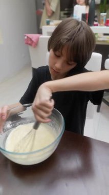 Parlak ve canlı bir mutfak ortamında, genç bir çocuk hamuru neşeyle karıştırma kabında çırpıyor.