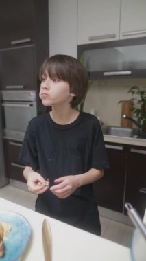 Genç bir çocuk, modern mutfak ortamında yaptığı leziz kreasyonları hem yemek pişirmekten hem de tatmaktan büyük keyif alır.