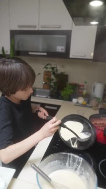 Genç bir çocuk krep yapmaktan zevk alır, yaratıcılığını ve yeteneklerini parlak, neşeli bir mutfakta gösterir.