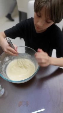 Genç bir çocuk, parlak ve renkli bir mutfak ortamında lezzetli bir hamuru çırpıcıyla karıştırmaktan zevk alır.