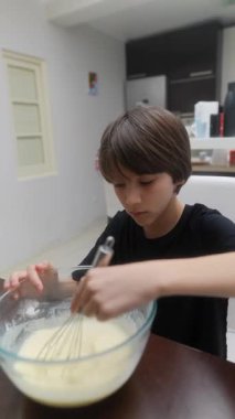 Sıcak ve modern bir mutfakta, genç bir çocuk büyük bir odaklanma ve enerjiyle mutlu ve özenle hamur çırpıyor.