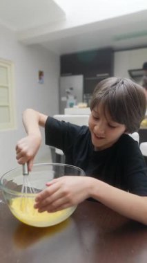 Bir çocuk neşeli bir şekilde bir kasede yumurta çırpıyor, birlikte yemek pişirmenin gerçek neşesini ve mutluluğunu gösteriyor.
