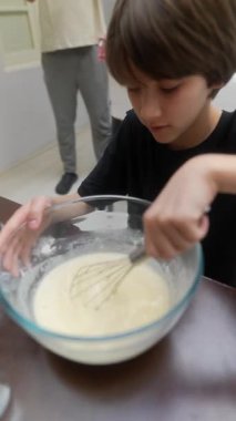 Genç bir çocuk hamuru bir kasede coşkuyla karıştırıyor, yemek yapma becerilerini ve neşeli yaratıcılığını sergiliyor..