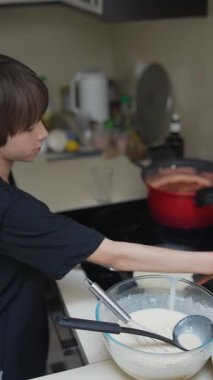 Şık bir mutfakta, genç bir çocuk hamuru coşkuyla karıştırır, aşçılık becerilerini ve yaratıcılığını gösterir.