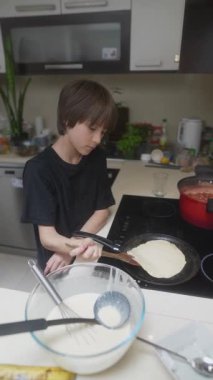 Bir çocuk güzel bir mutfakta krep pişiriyor, mutfak yeteneklerini sergiliyor ve eğleniyor.