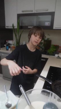 Genç bir çocuk, modern bir mutfak ortamında çeşitli malzemeleri ustalıkla birleştirip yemek pişirmekten zevk alır.