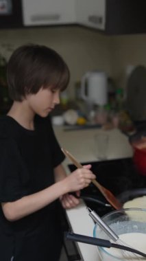 Genç bir çocuk zevkle renkli bir hamuru kaynayan modern bir mutfakta lezzetli yemekler yapmak için karıştırır.