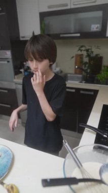 Mutlu ve neşeli bir çocuk herkes için sıcak, neşeli ve modern bir mutfakta krep yapmakla meşgul.