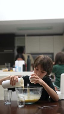 Bir çocuk neşe içinde mutfakta yardım eder, aile lezzetli yemekler hazırlarken malzemeleri kaseye döker.