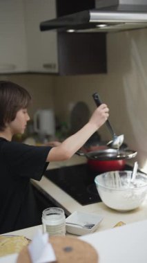 Genç bir çocuk, mutfak yaratıcılığını gösteren modern bir mutfakta zevkle yemek pişirir ve deneyler yapar.