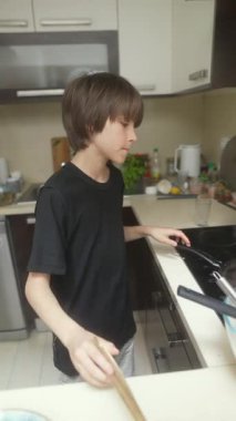 Genç bir çocuk, çağdaş bir mutfaktaki aşçılık sürecinin tadını çıkarırken ustaca krep pişiriyor..