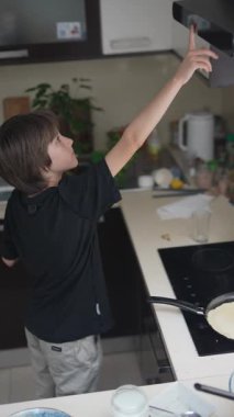 Genç bir çocuk neşeli ve coşkulu bir şekilde ahşap bir kaşık kullanarak neşeli ve neşeli bir mutfakta yemek pişiriyor.