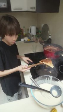 Genç bir çocuk, parlak ve modern bir mutfakta ustaca krep pişiriyor. Mutfak yeteneklerini sergiliyor.