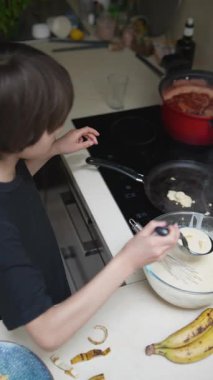 Genç bir çocuk heyecanlı bir şekilde mutfakta krep yapıyor, ailesini etkilemek için yaratıcılığını ve becerilerini gösteriyor.
