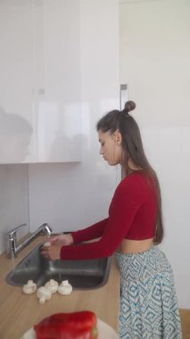 Bir kadın lavaboda taze, renkli sebzeler hazırlıyor ve sağlıklı yemek yapmanın önemini vurguluyor.
