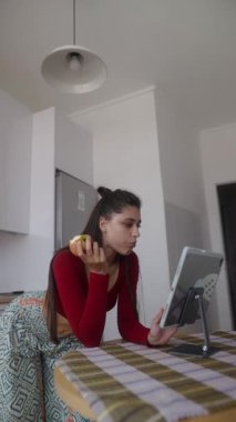Bir kadın, şık ve şık bir mutfak ortamında tabletine odaklanırken atıştırmalıktan zevk alır.